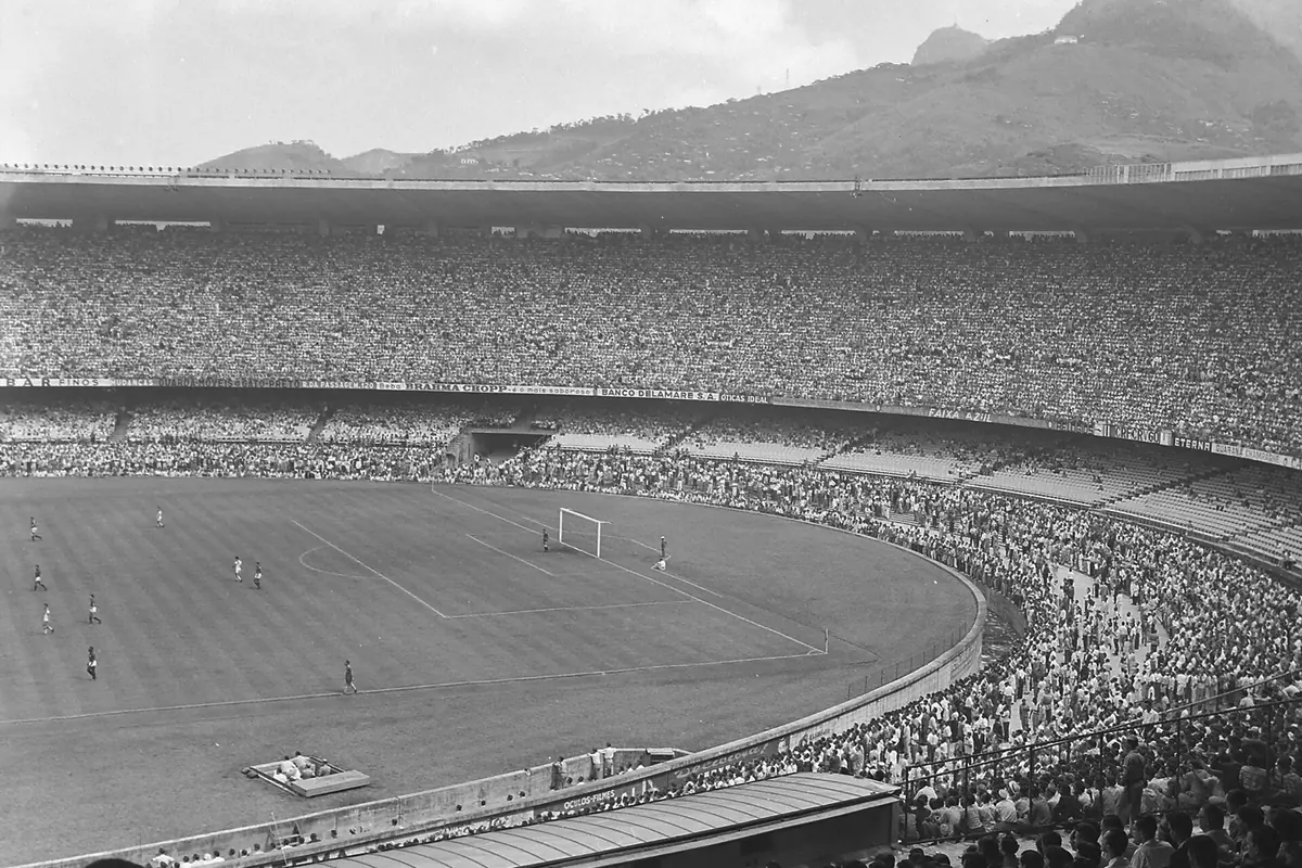 A black-and-white photograph of a match in the Maracanã before the 1950 World Cup, with crowds filling the terraces and a mountain beyond the stadium