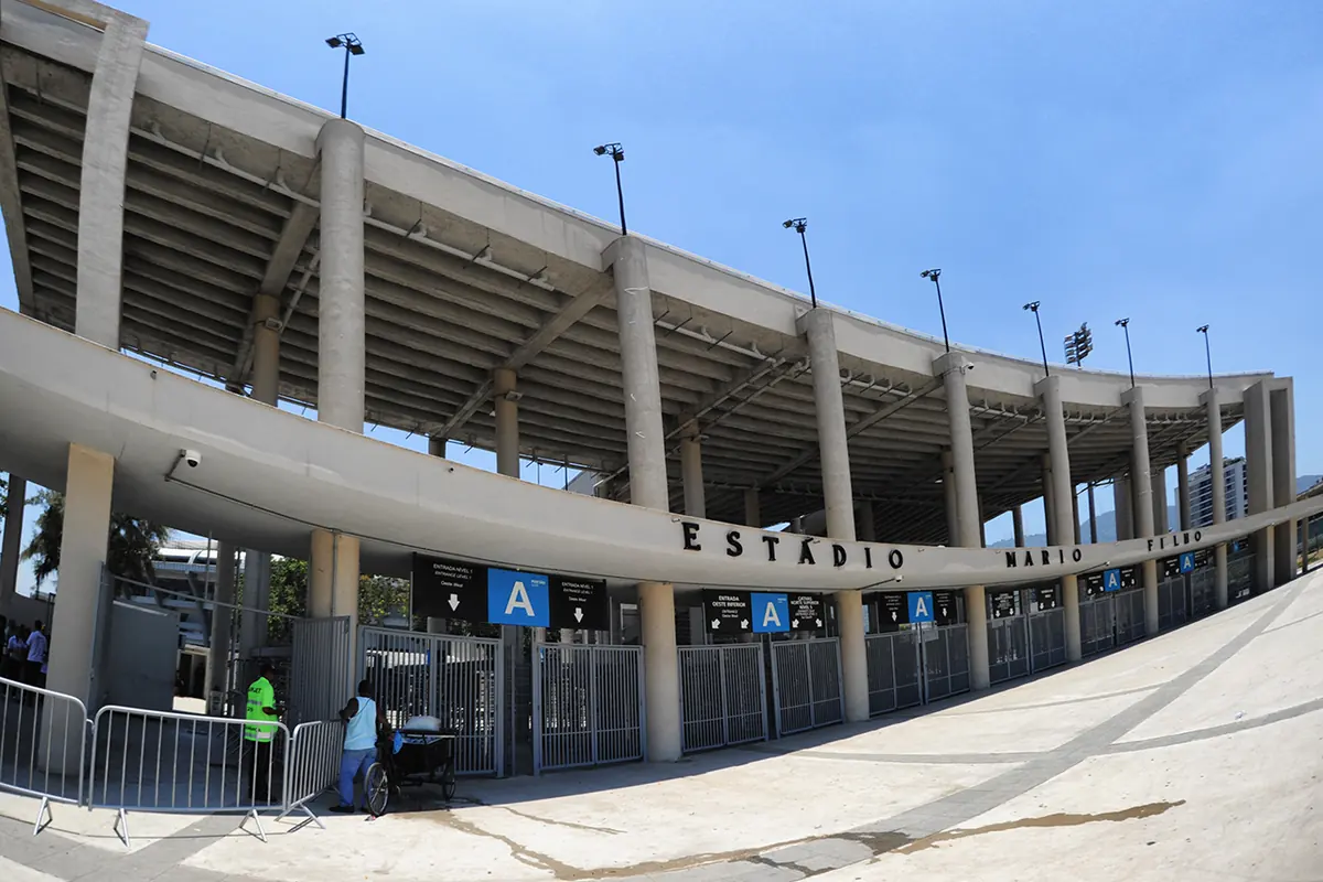 The curved concrete frontage of the Maracanã on a sunny day, with a blue entrance sign marked A and palm trees along the plaza