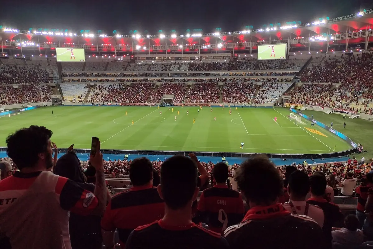 A match at the Maracanã with the stands full of fans in red and black beneath the roof, seen from the upper tier
